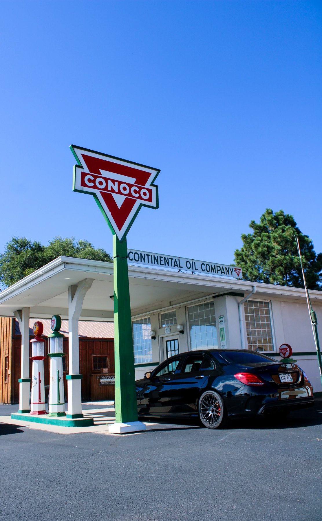 Black Mercedes-AMG sedan parked at a vintage Conoco gas station