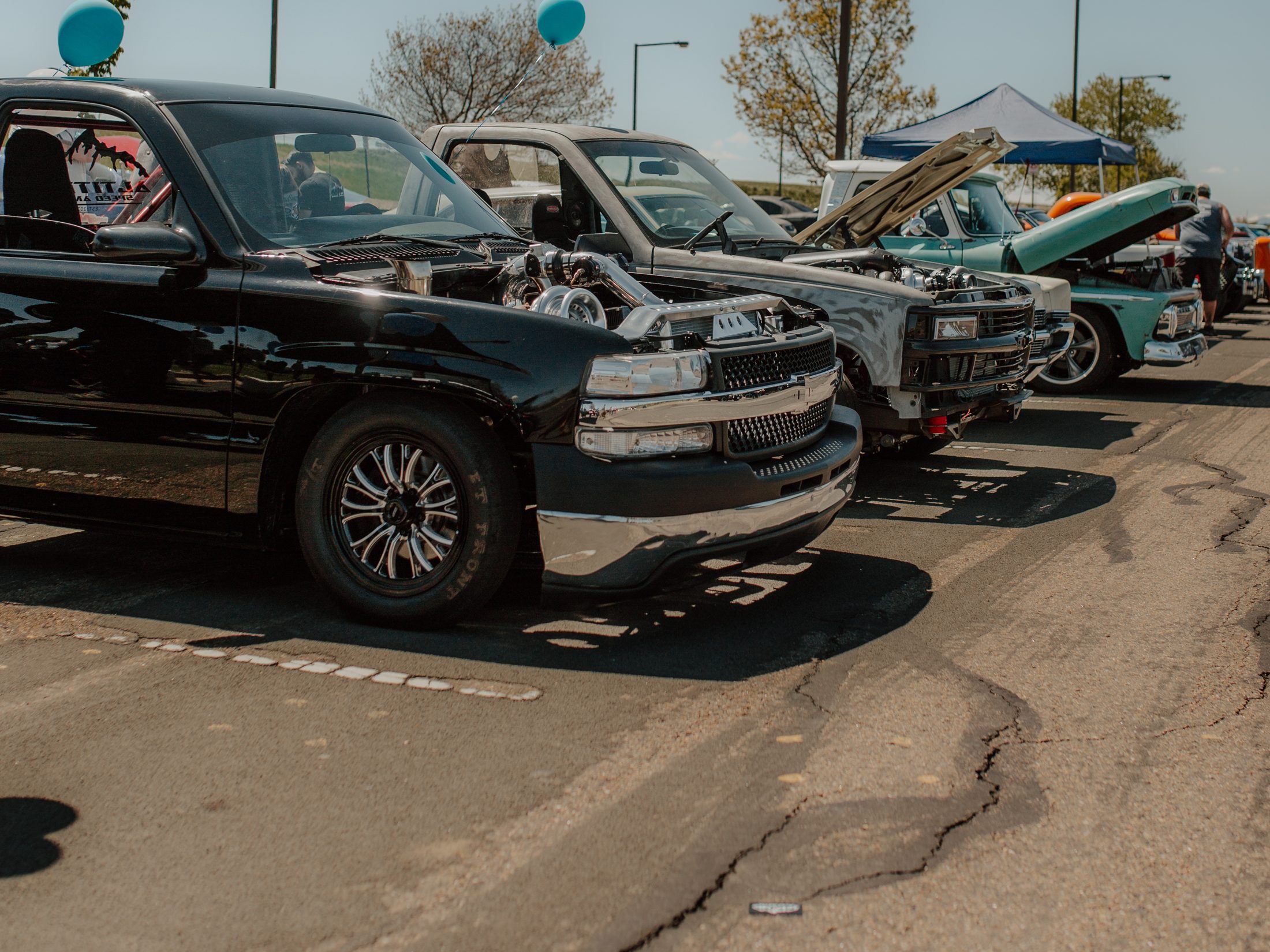 Shop trucks lined up with their hoods open at a car show