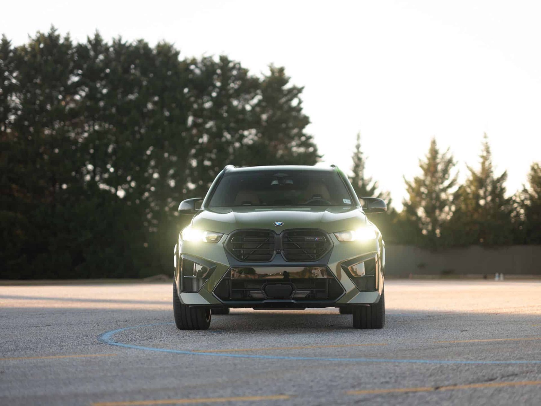 Green BMW X5 M seen head-on with its headlights on
