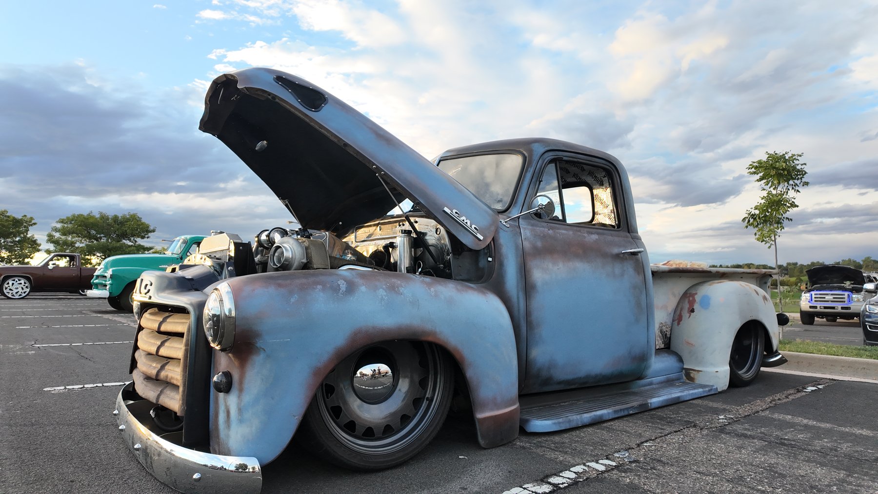 Lowered patina GMC pickup with the hood up showing a turbo engine