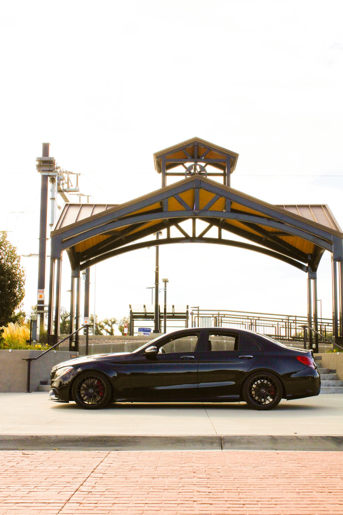Black Mercedes-AMG sedan in profile in front of a timber pavilion