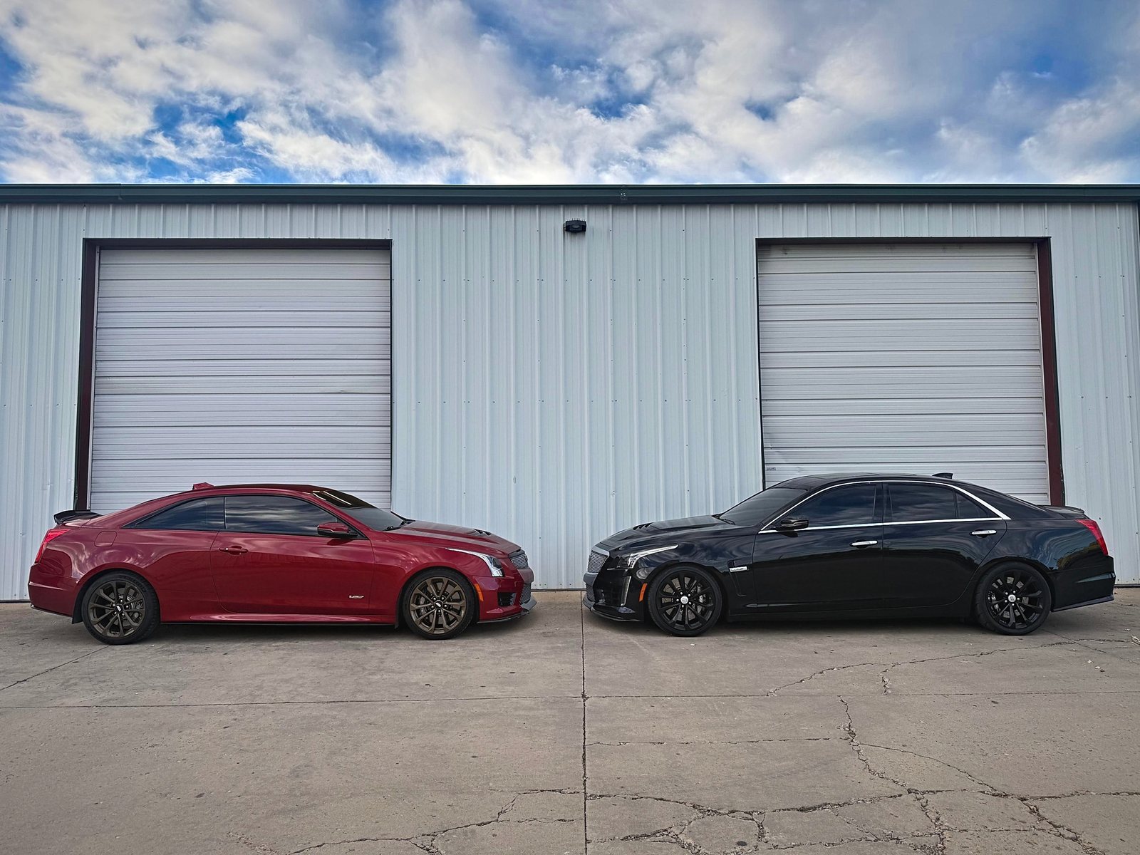 Red Cadillac ATS-V coupe and black CTS-V sedan parked nose to nose outside the shop